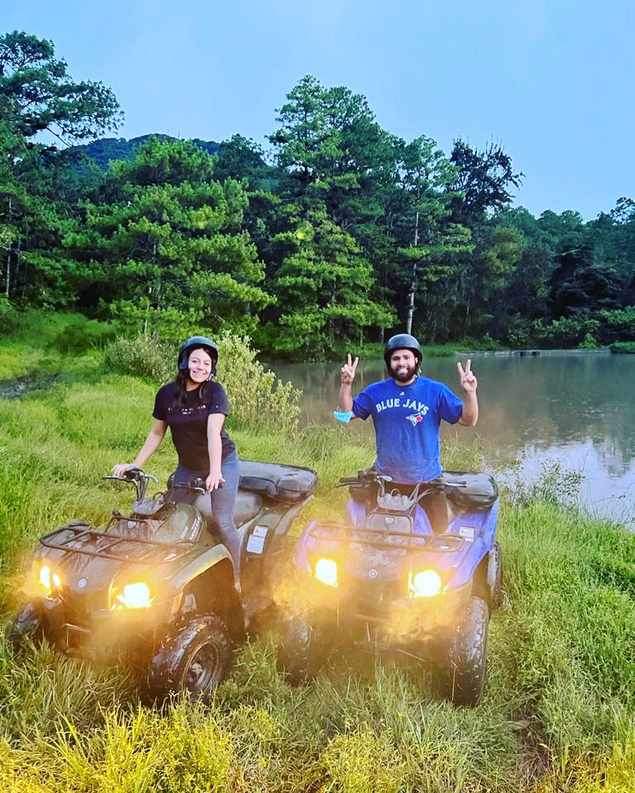 Two riders on ATVs beside a pond in the forest