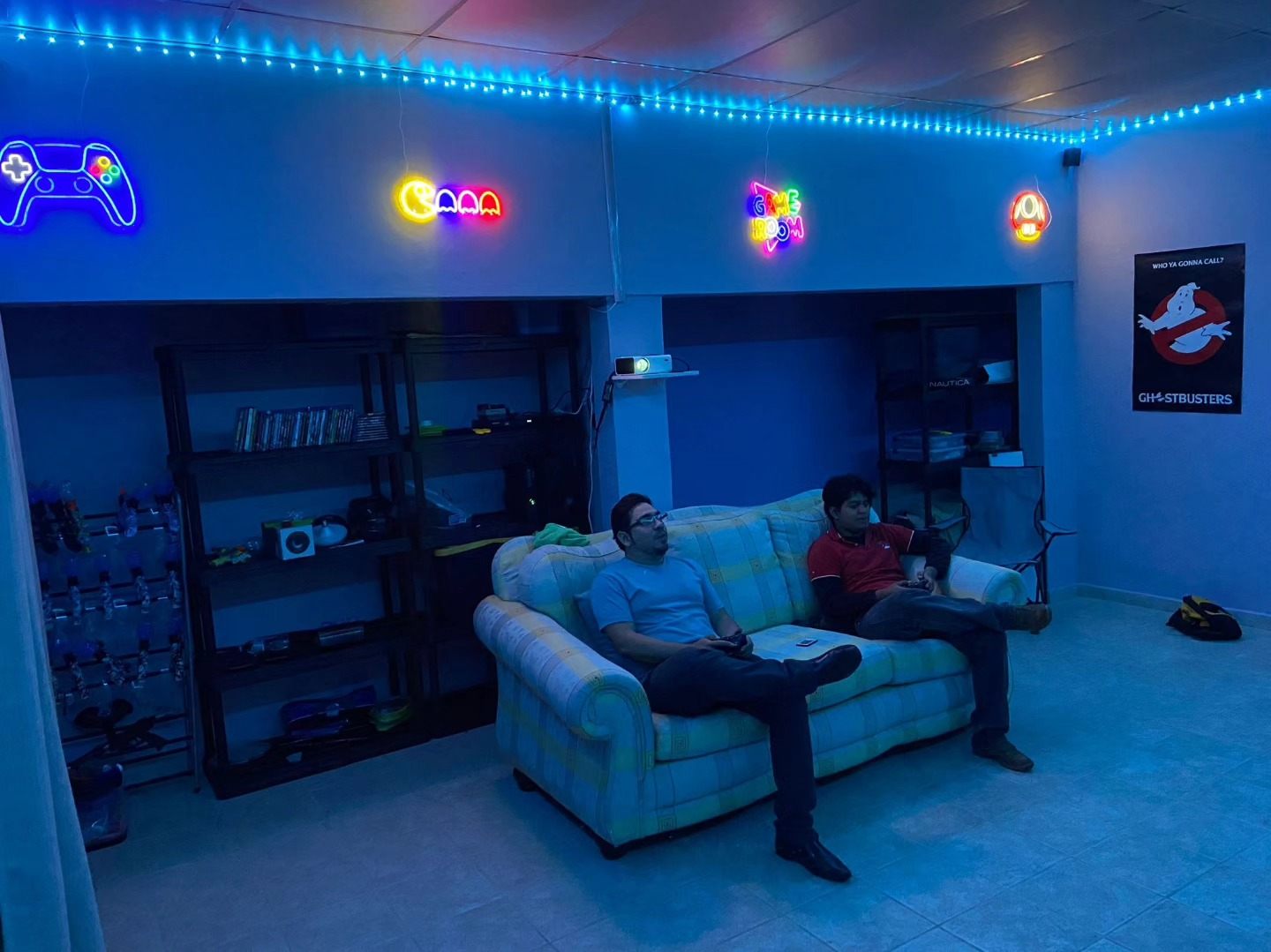 Game room lit in blue neon with sofa, arcade lights and shelves