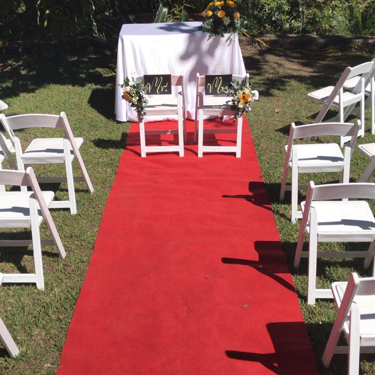 Garden wedding ceremony with a red carpet aisle between white chairs